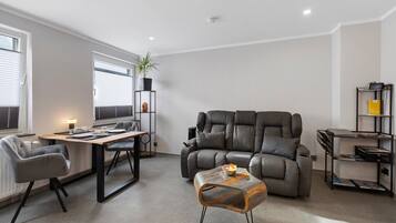 Ein modernes Wohnzimmer mit einer Ledersofa, einem Esstisch mit Stühlen, einem kleinen Couchtisch und einem Bücherregal.