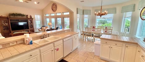 A spacious kitchen with a large island, a dining area with a chandelier, and a view of the outdoors through large windows.