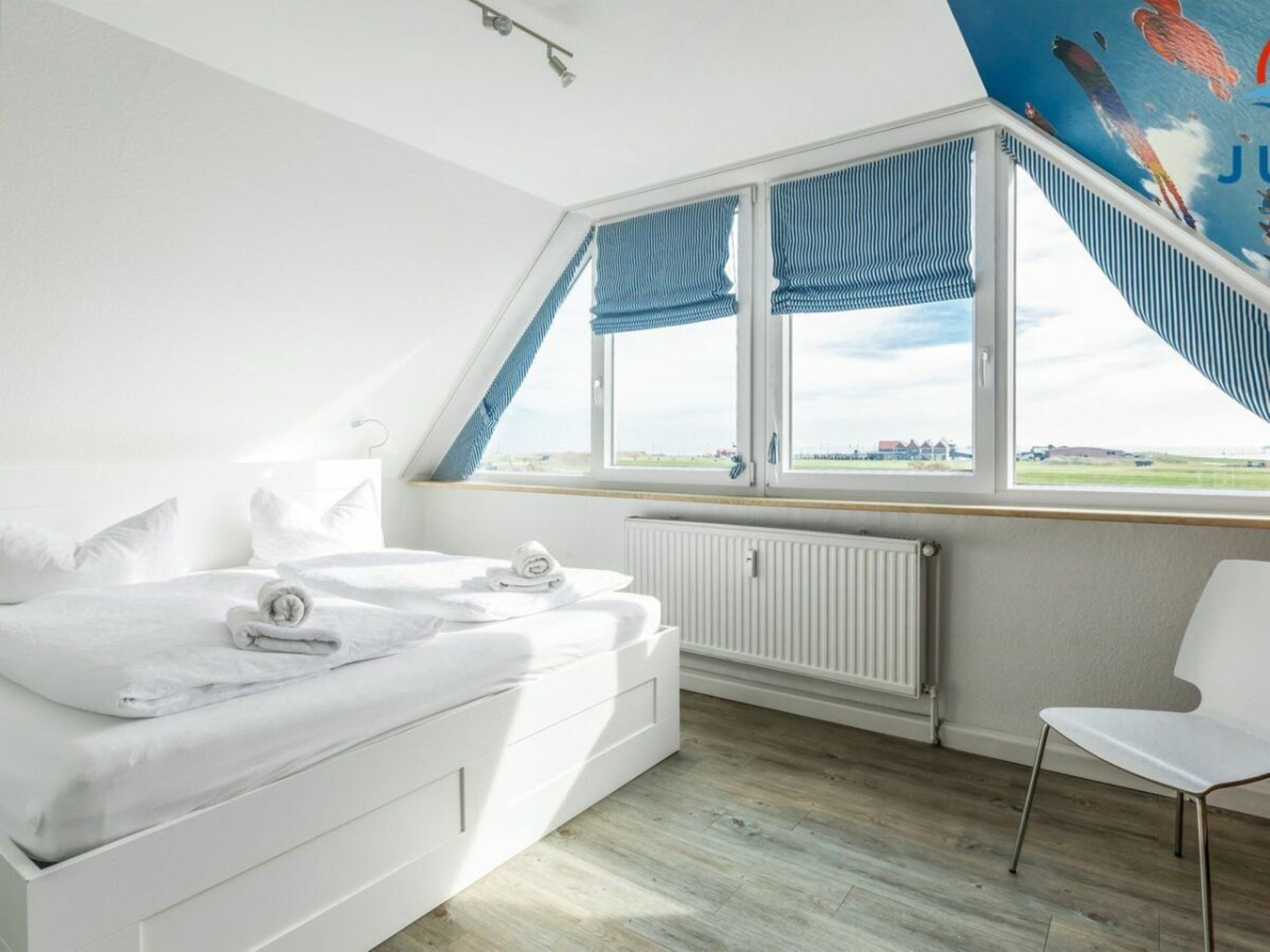 Quarto com cama, radiador, janela com cortinas e vista para a paisagem.