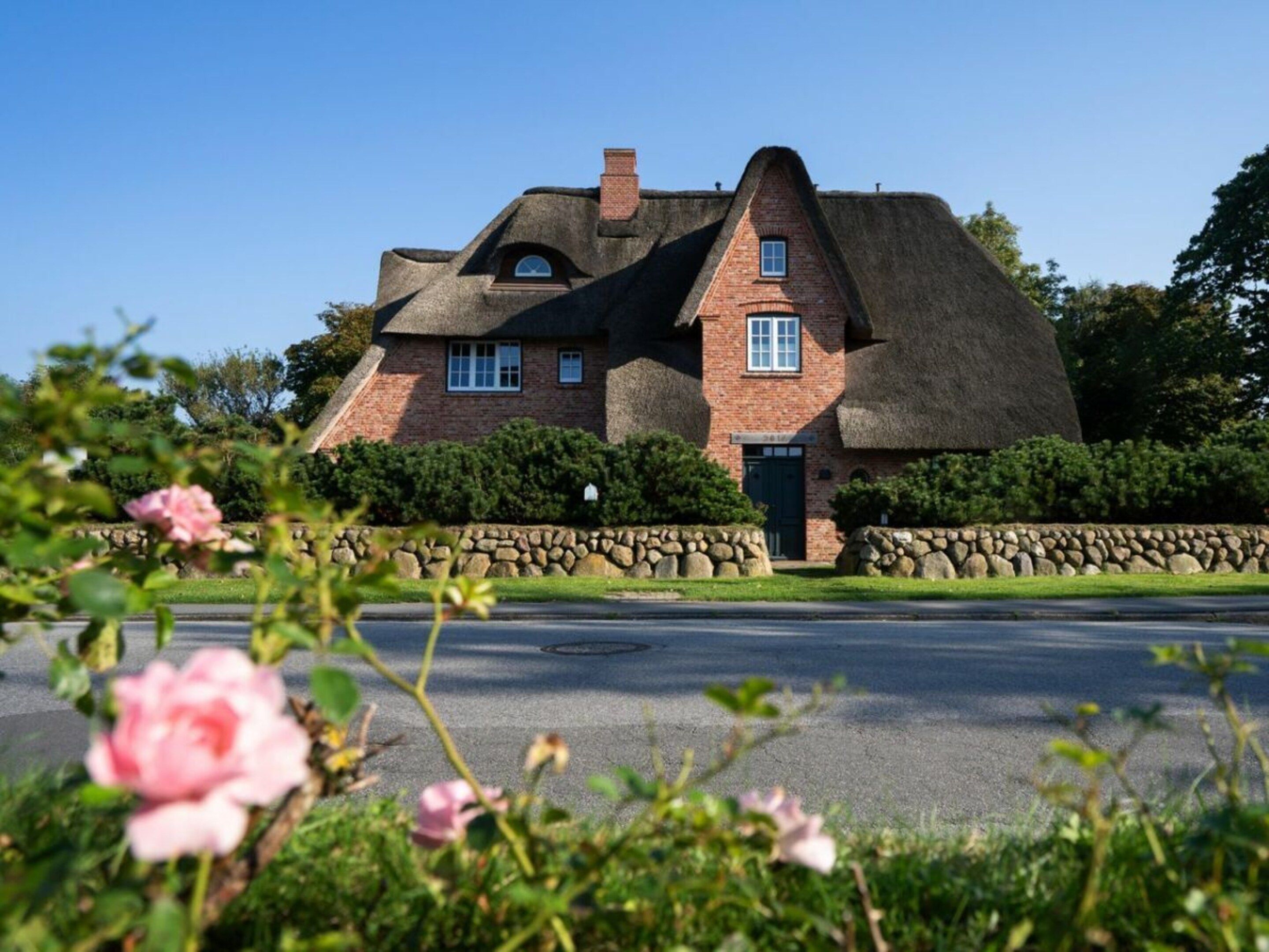 A house with a thatched roof, brick walls, and a stone wall in front.