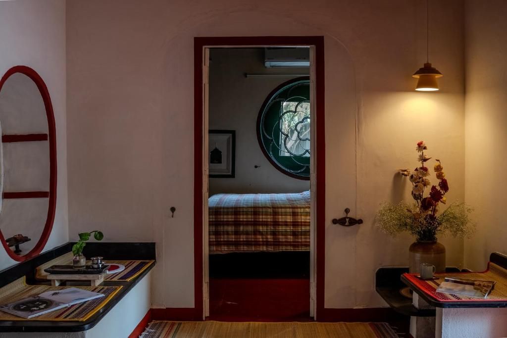 Una habitación con cama, escritorio con papeles, un jarrón con flores y ventana con vistas.