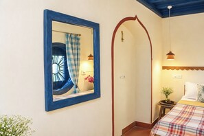 Un dormitorio con cama, mesita de noche, espejo, ventana con cortinas y lámpara en el techo.
