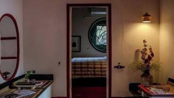 A room with a bed, a mirror, a vase with flowers, and a window with a circular design.
