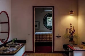 A room with a bed, a mirror, a vase with flowers, and a window with a circular design. - Maison Verona Pool Villa Pondicherry (Kottakuppam)