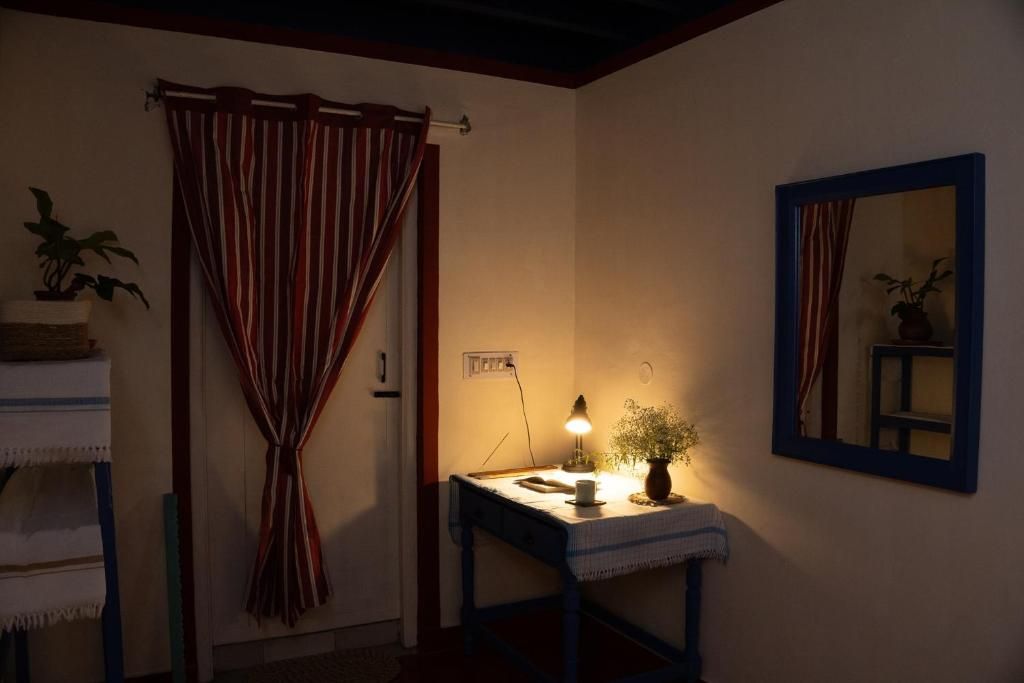 A room with a bed, a bedside table with a lamp, a mirror, and a window with curtains.