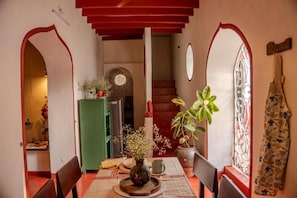 Un comedor con una mesa dispuesta para dos personas, un aparador verde, un reloj y una escalera que conduce a un nivel superior.