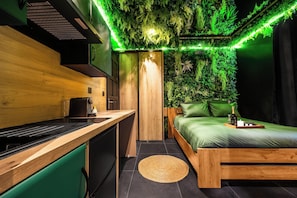 Un dormitorio moderno con una pared verde, una cama de madera y una zona de cocina con estufa.