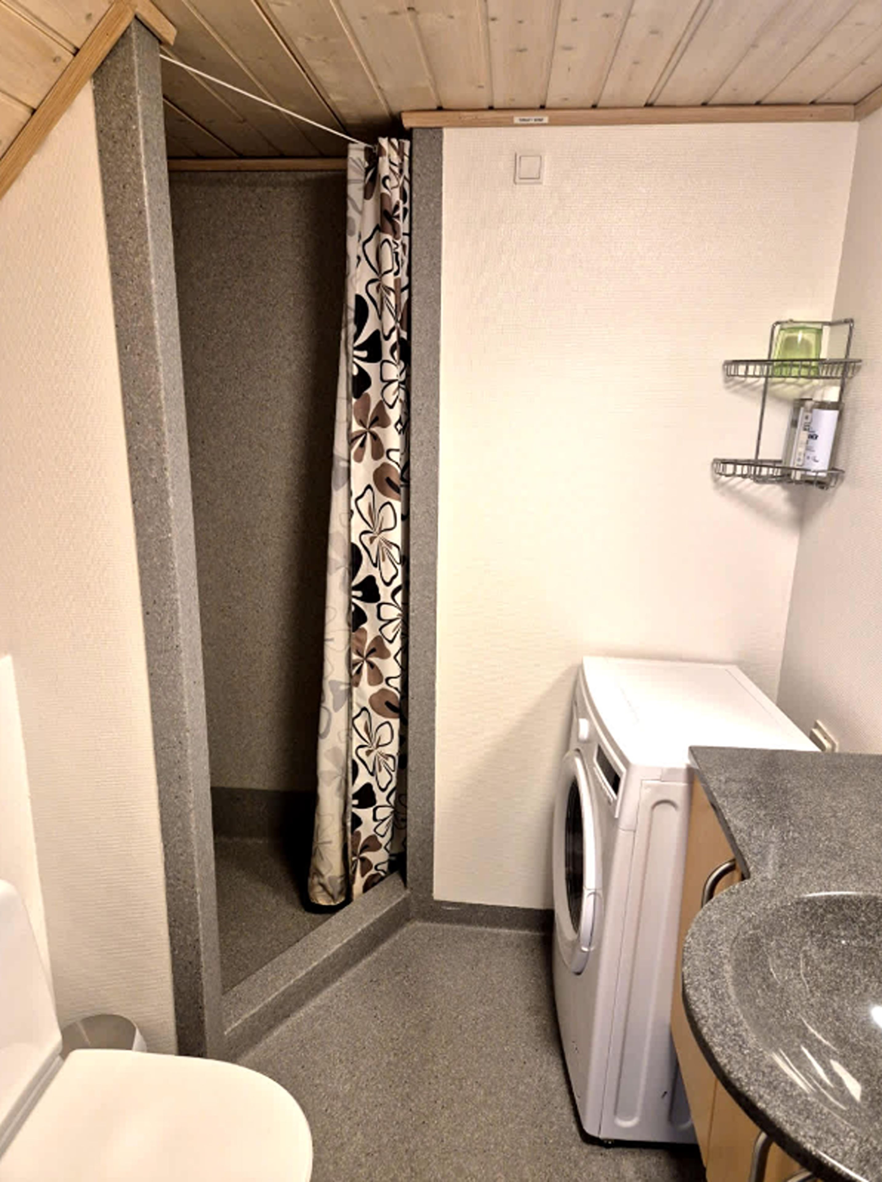 A compact laundry room with a washing machine, a shower curtain, and a small shelf with toiletries.