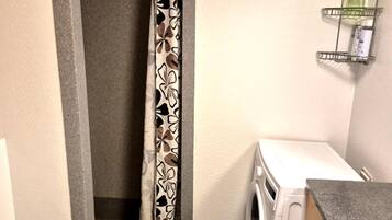 A compact laundry room with a washing machine, a shower curtain, and a small shelf with toiletries.