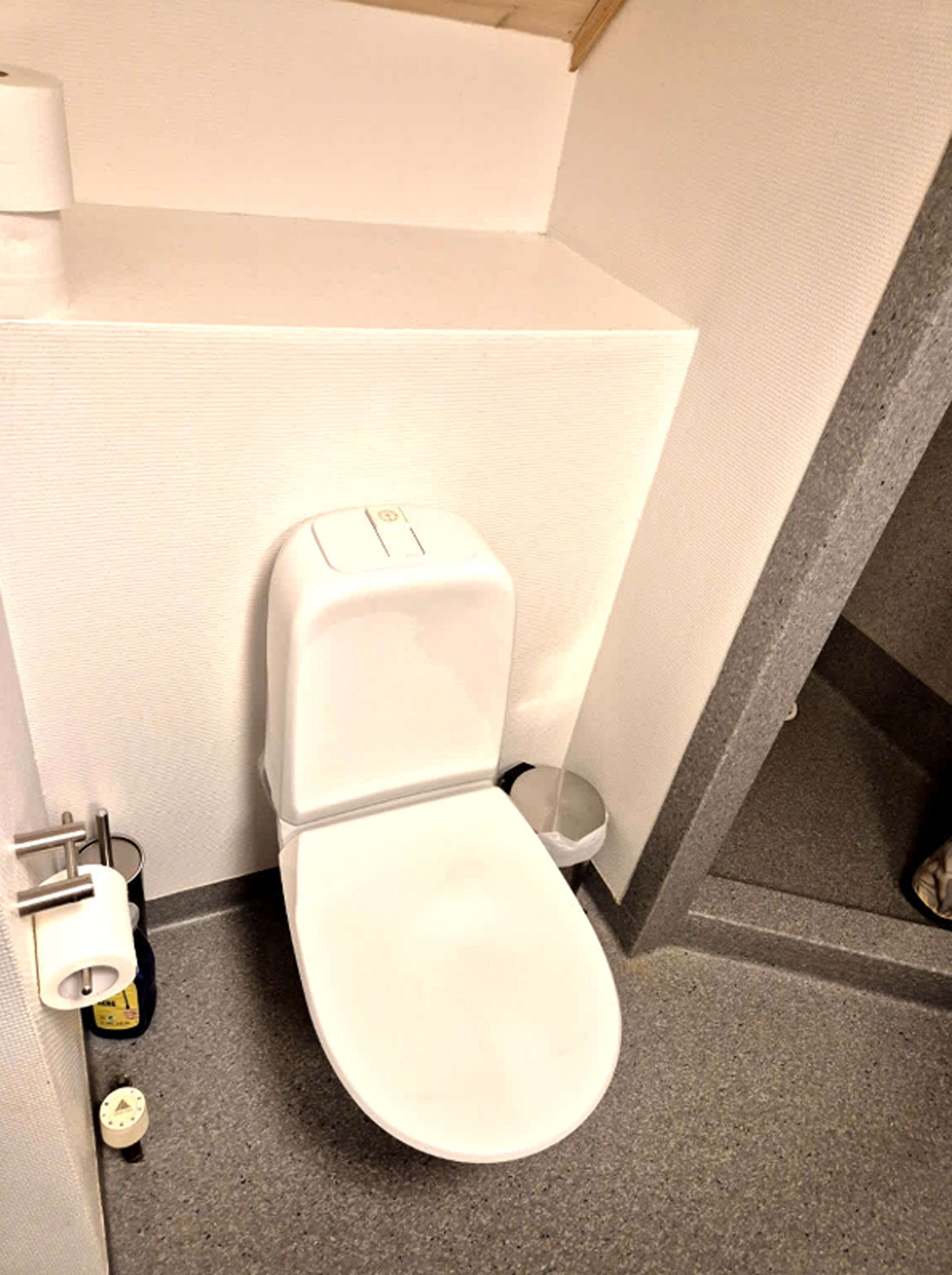 Un baño pequeño y funcional con inodoro blanco, dispensador de papel higiénico y cubo de basura.