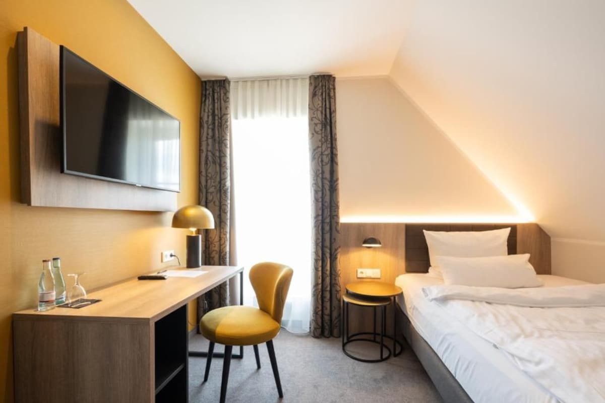 Une chambre d’hôtel comprenant un lit, un bureau avec une chaise, un téléviseur fixé au mur et une lampe.