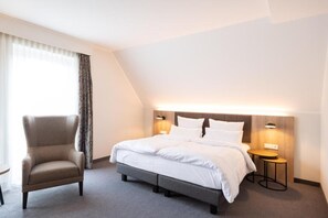 Une chambre d’hôtel avec un lit, des tables de chevet, une chaise et une fenêtre avec des rideaux.