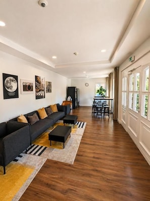 Un hall d’hôtel moderne avec un canapé noir, un plancher en bois et un coin repas à l’arrière-plan.