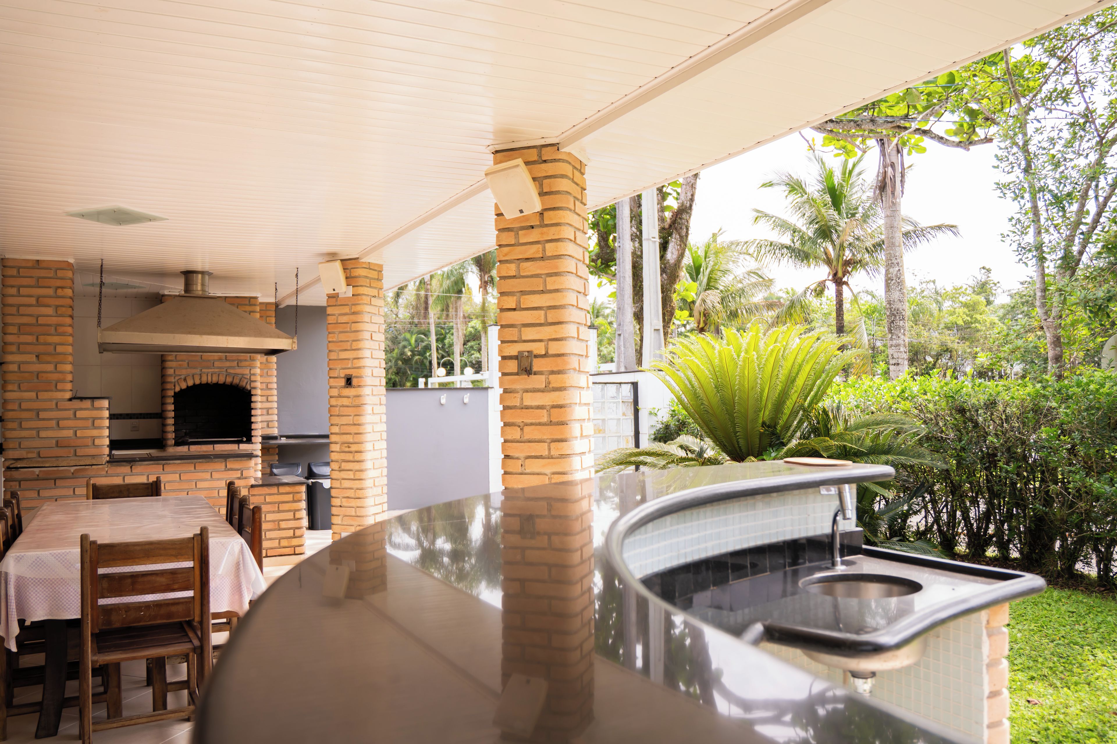An outdoor kitchen area with a brick oven, a table with chairs, and a view of the surrounding greenery.