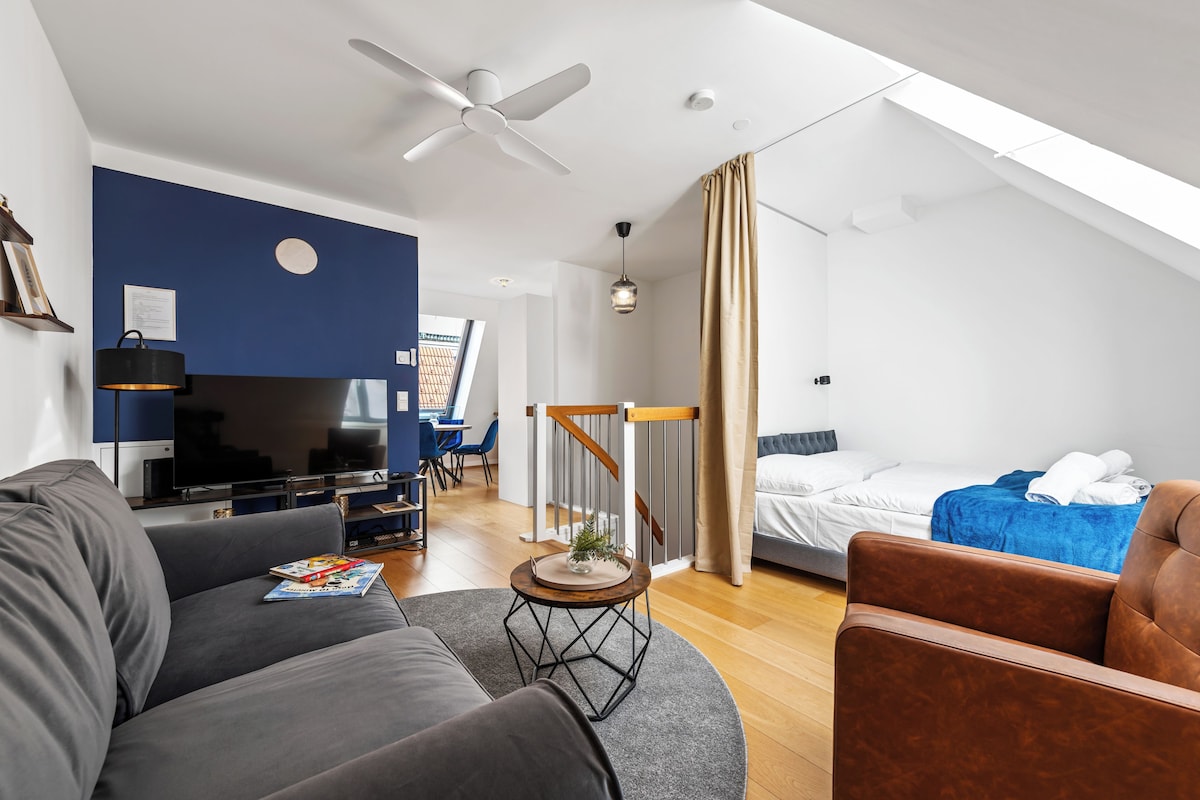 Een moderne woonkamer met een flatscreen televisie, een plafondventilator en een eethoek met blauwe stoelen.