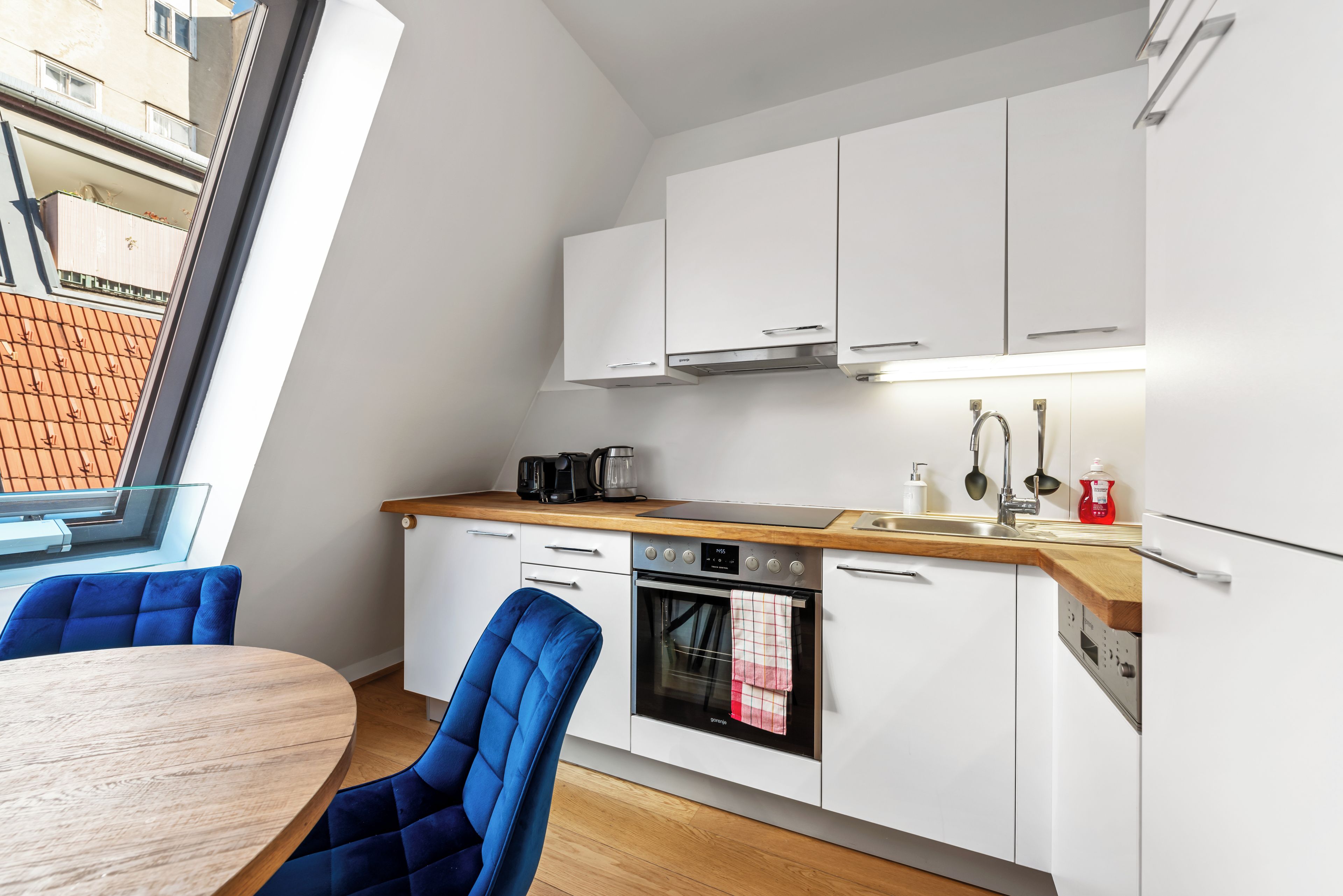 Een moderne keuken met witte kasten, een houten aanrechtblad, een inbouwoven en een eethoek met blauwe stoelen.