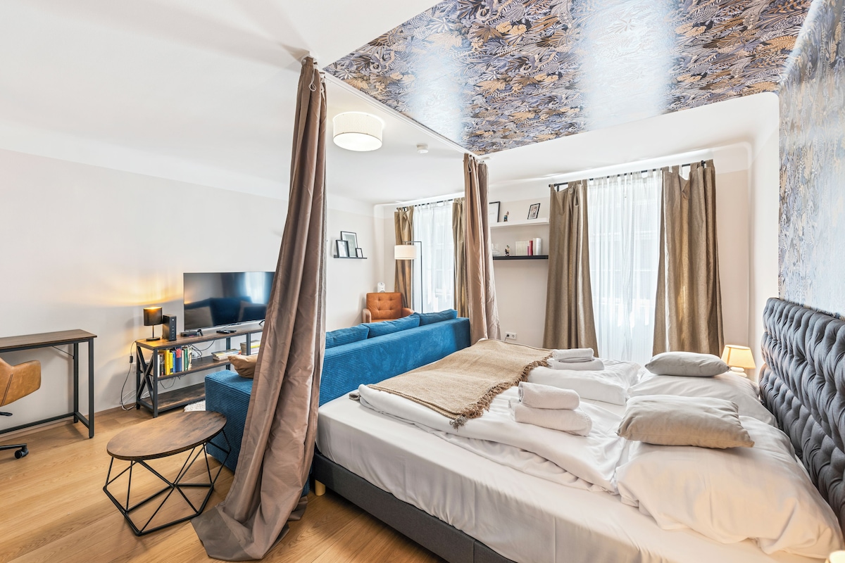 Een moderne slaapkamer met een groot bed, een bureau met een computer, een stoel en een blauwe bank.