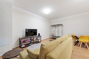 Een moderne woonkamer met een bank, een televisie, een eettafel met stoelen en een boekenkast.