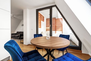 Een moderne kamer met een ronde houten tafel, blauwe fauteuils en een groot raam met houten luiken.