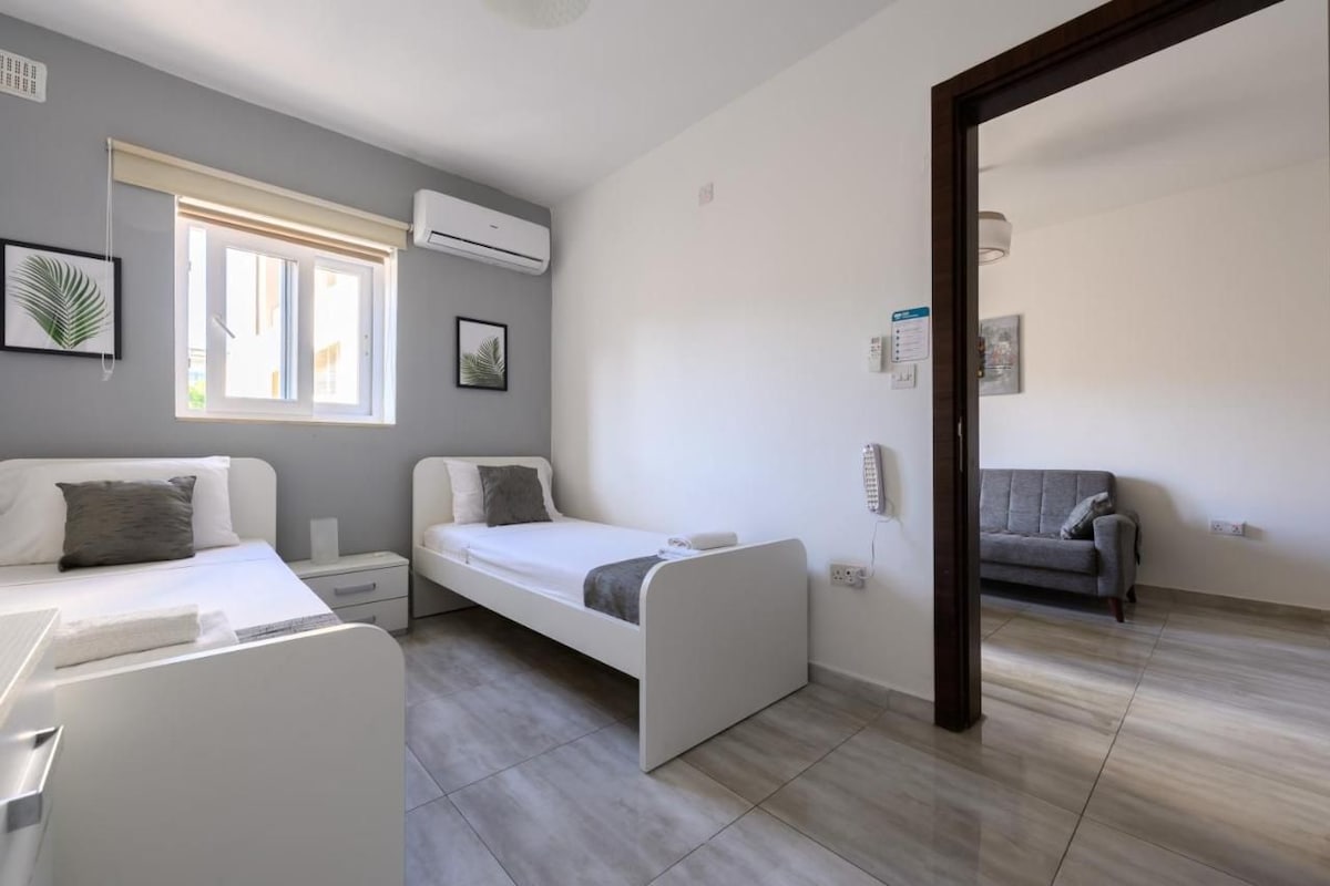 Ein modernes Schlafzimmer mit einem Bett, Nachttischen, einem Sofa und einem Fenster mit Jalousien.