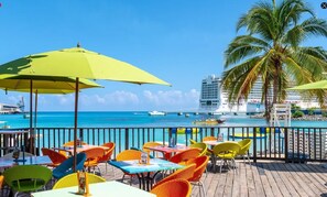 Un restaurante frente al mar con terraza, vistas al océano y una palmera.