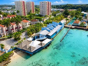 Un resort costero con bungalows sobre el agua, un puerto deportivo y edificios altos en el fondo.