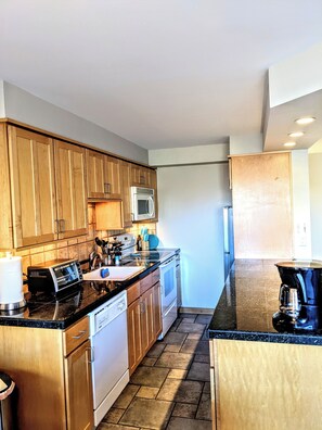 A modern kitchen with wooden cabinets, stainless steel appliances, and a black countertop. - 30 Day+ Quiet, 2 BR/1 BA Condo in Congress Park (Denver)