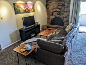 Ett vardagsrum med en öppen spis, en soffa, ett soffbord och en tv.