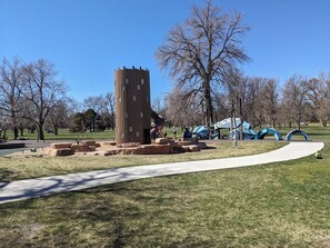 A park with a tall wooden structure, a playground with blue slides, and a paved walkway. - 30 Day+ Quiet, 2 BR/1 BA Condo in Congress Park (Denver)