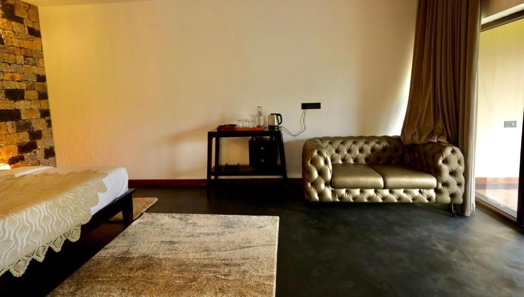 Una habitación con cama, sofá, una mesita con hervidor y pared de piedra.