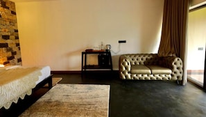 Una habitación con cama, sofá, una mesita con hervidor y pared de piedra.