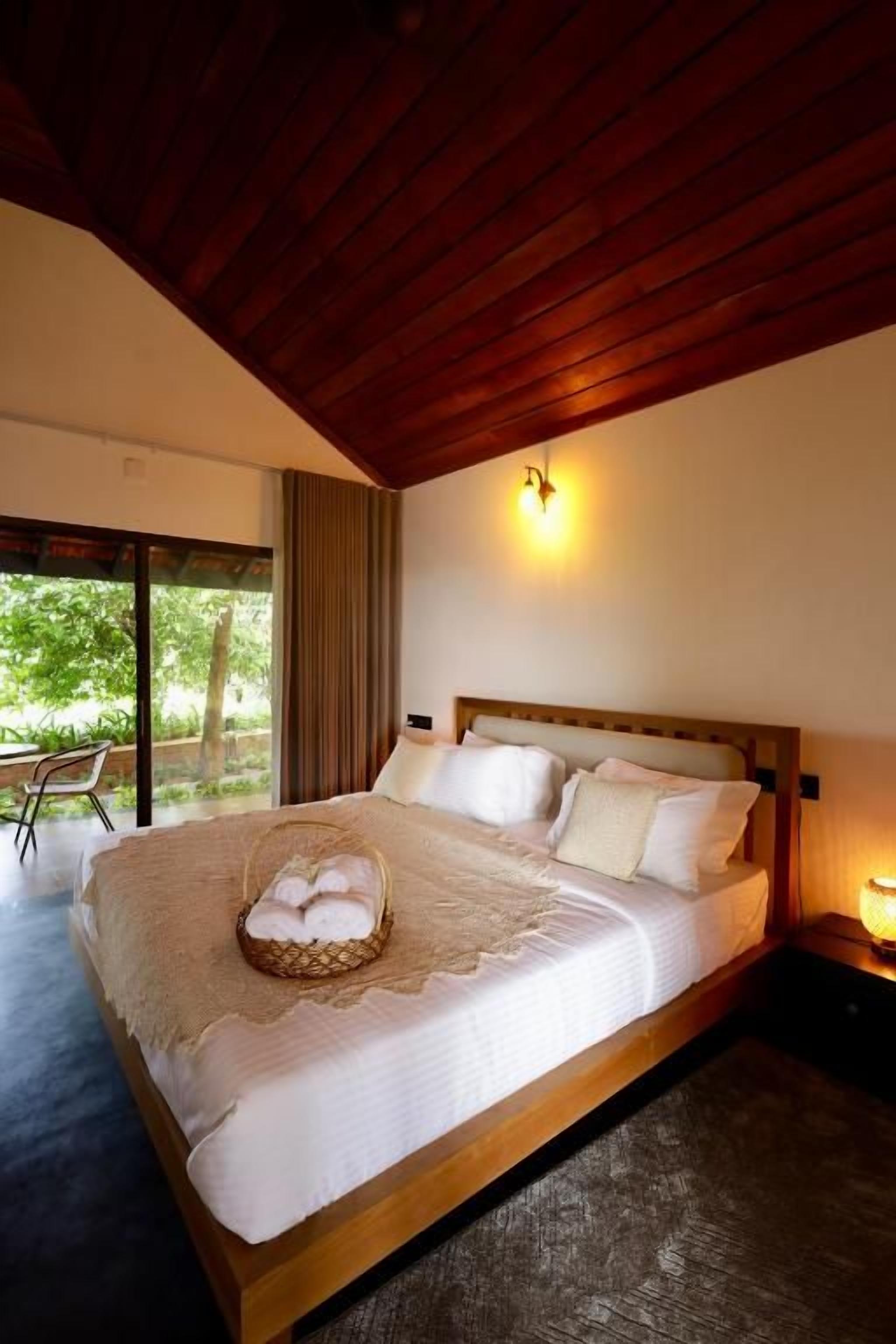Una cama grande con cabecera de madera, una lámpara de noche y una cesta de toallas.