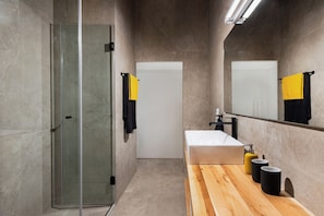 A modern bathroom with a glass shower enclosure, a white sink, and a wooden vanity. - Art Space Residencies Α1 (Athina)