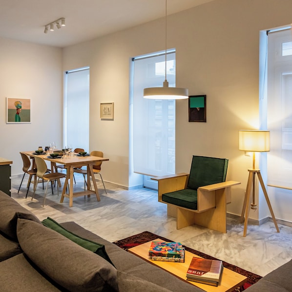 A modern living room with a dining area, a green armchair, a floor lamp, and artwork on the walls. - Art Space Residencies Α1 (Athina)