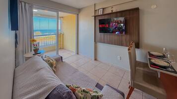 Una sala de estar con sofá, televisión instalada en la pared, balcón con vistas y zona de comedor con mesa.