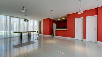 Un amplio y moderno vestíbulo de hotel con una pared de acento roja, una recepción y un gran ventanal con cortinas translúcidas.