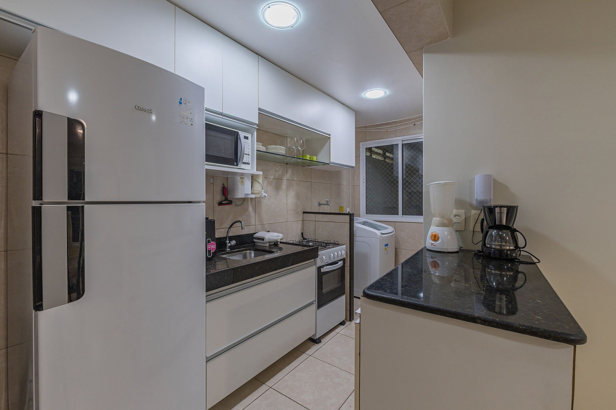Una cocina moderna con refrigerador, microondas, pileta, estufa y cafetera.