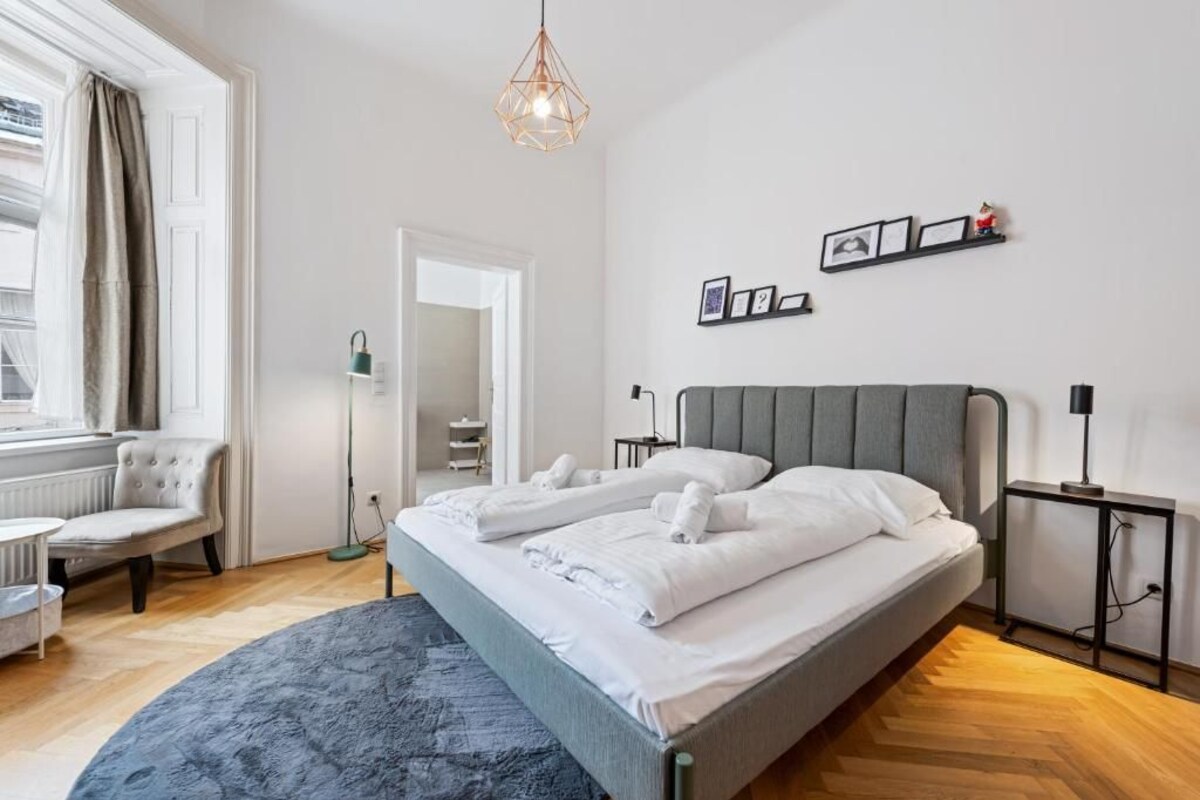 Een hotelkamer met een bed, nachtkastjes, een stoel, een vloerlamp en een raam met gordijnen.