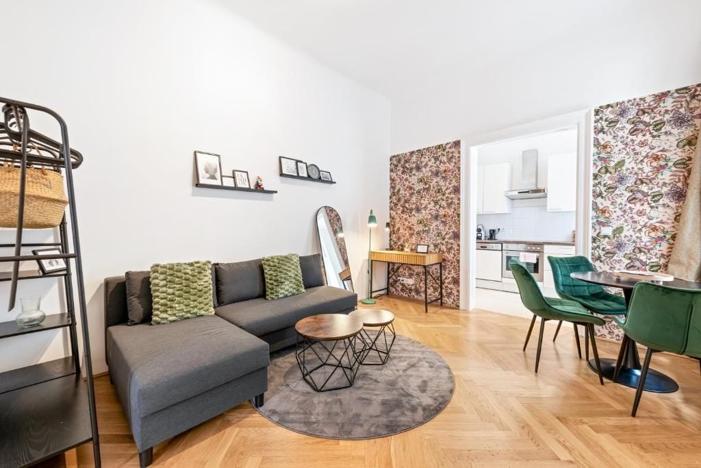 Una sala moderna con sofá, mesa de centro y sillas, un área de cocina con armarios y una mesa de comedor, y una pared con diseño.