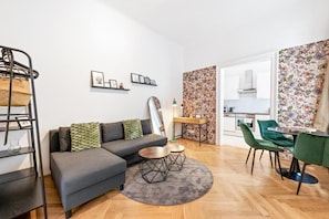 Een moderne woonkamer met een bank, salontafel en stoelen, een keuken met kastjes en een eettafel, en een behang met een patroon.