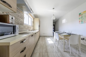 Cocina moderna con horno integrado, microondas y lavaplatos, que da paso a un comedor con mesa y sillas.