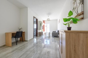 Amplia sala de estar con un escritorio de madera, una silla negra, un sofá gris y un mueble de madera.