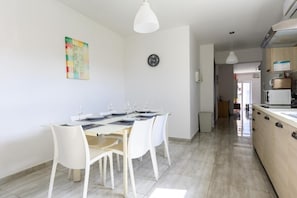 Et moderne køkken med en central ø, et spiseområde med et bord dækket til fire, og et ur på væggen.
