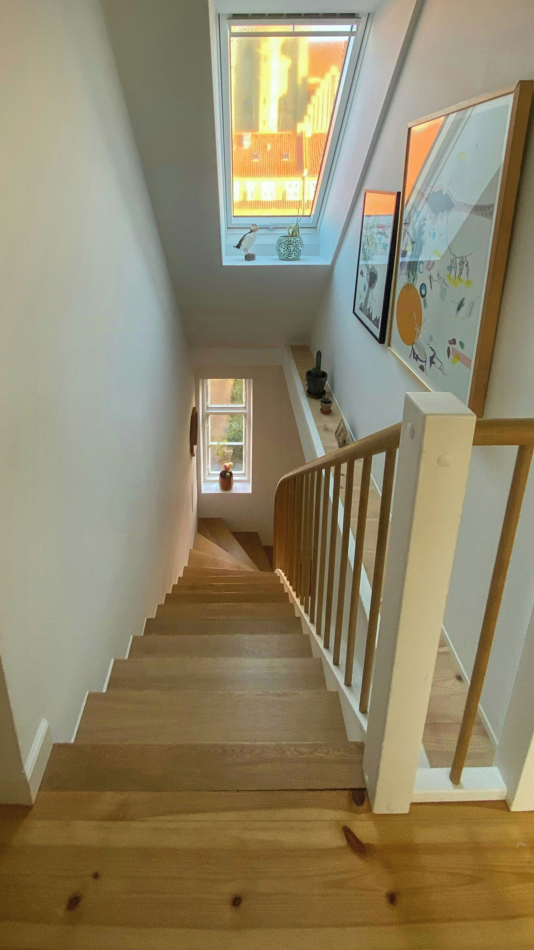 A wooden staircase with a white railing leading to a landing with a skylight.