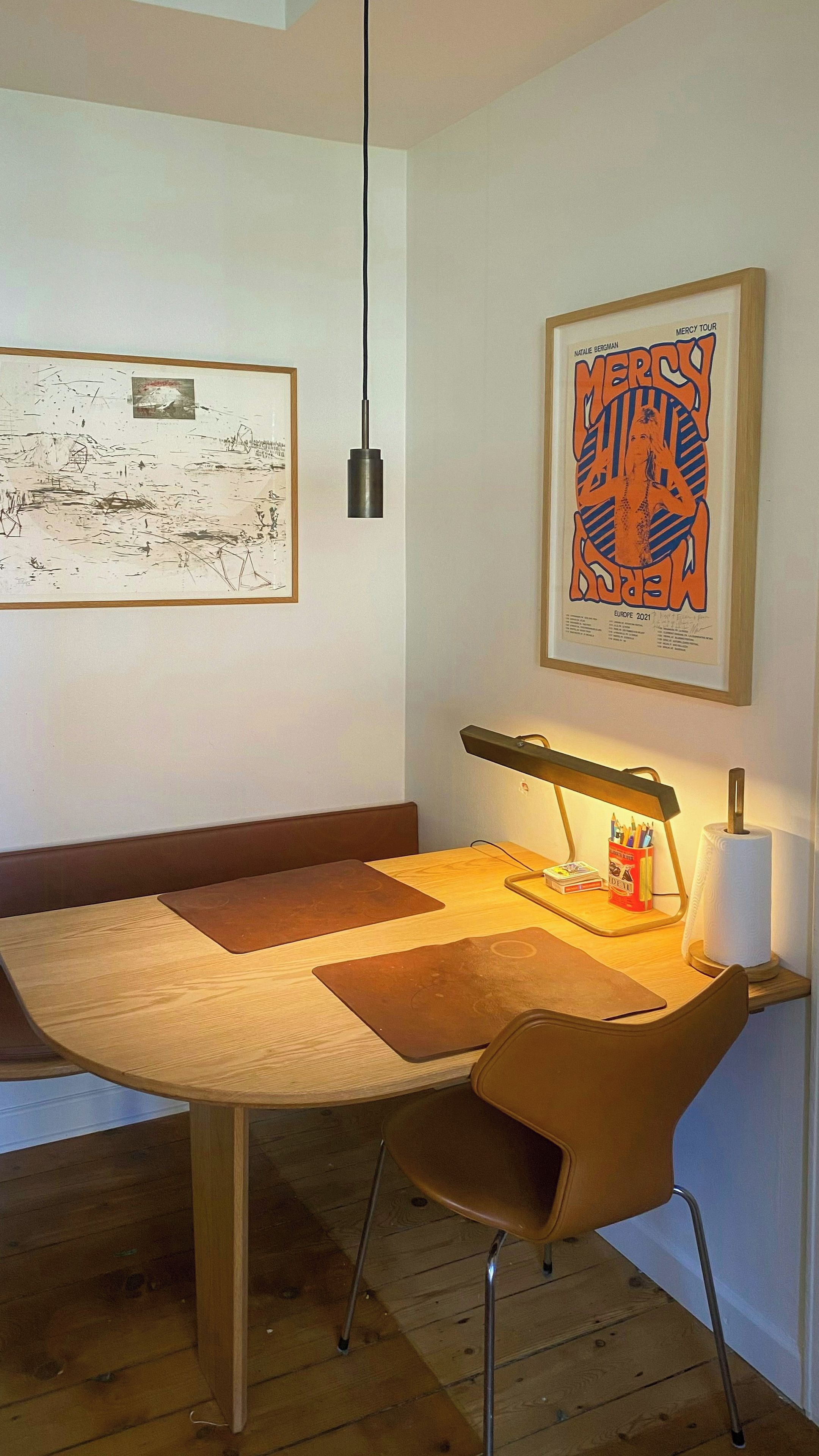 A dining area with a wooden table, a modern lamp, and artwork on the walls.