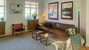 Sala de estar com sofá de couro marrom, mesa de centro de madeira, cadeira de madeira pequena, abajur e um cão.
