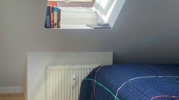 A small, well-lit attic bedroom with a skylight, a radiator, a bed with a quilt, and a rug on the floor.