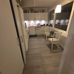 Une cuisine compacte avec des meubles blancs, un coin repas comprenant une table et des chaises, et une fenêtre offrant une vue agréable.