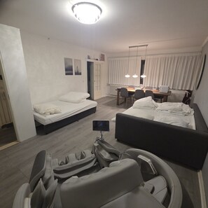 Une chambre d’hôtel comprenant un lit, un fauteuil massant, un bureau avec une chaise et un coin repas avec une table et des chaises.