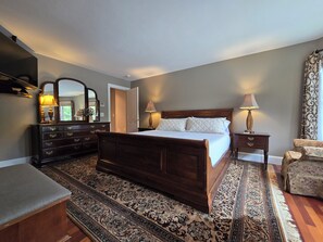 Um quarto com cama de madeira, mesas de cabeceira com luminárias, cômoda, cadeira e tapete estampado.